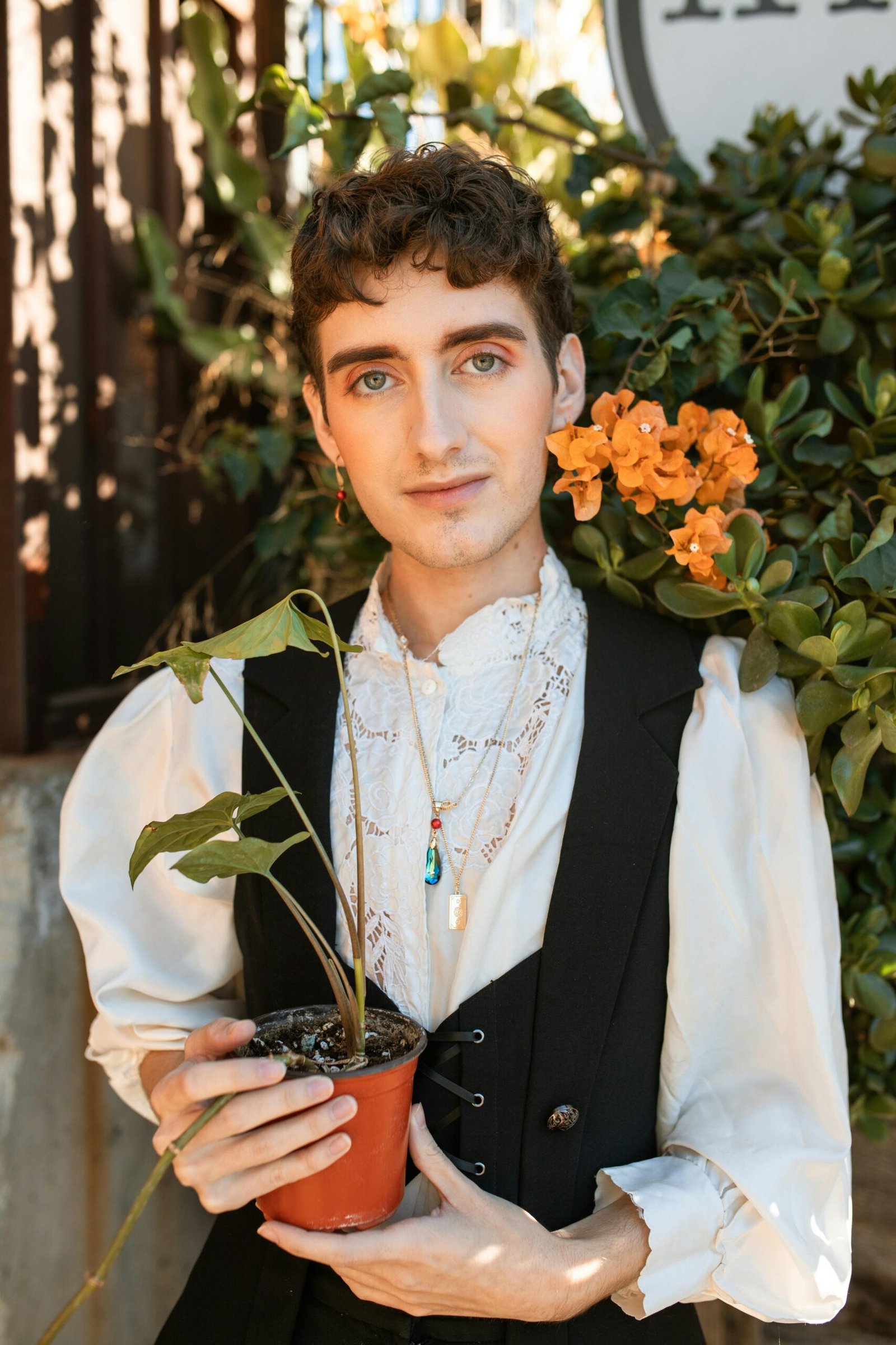 A stylish young adult poses with a potted plant against a floral backdrop.
